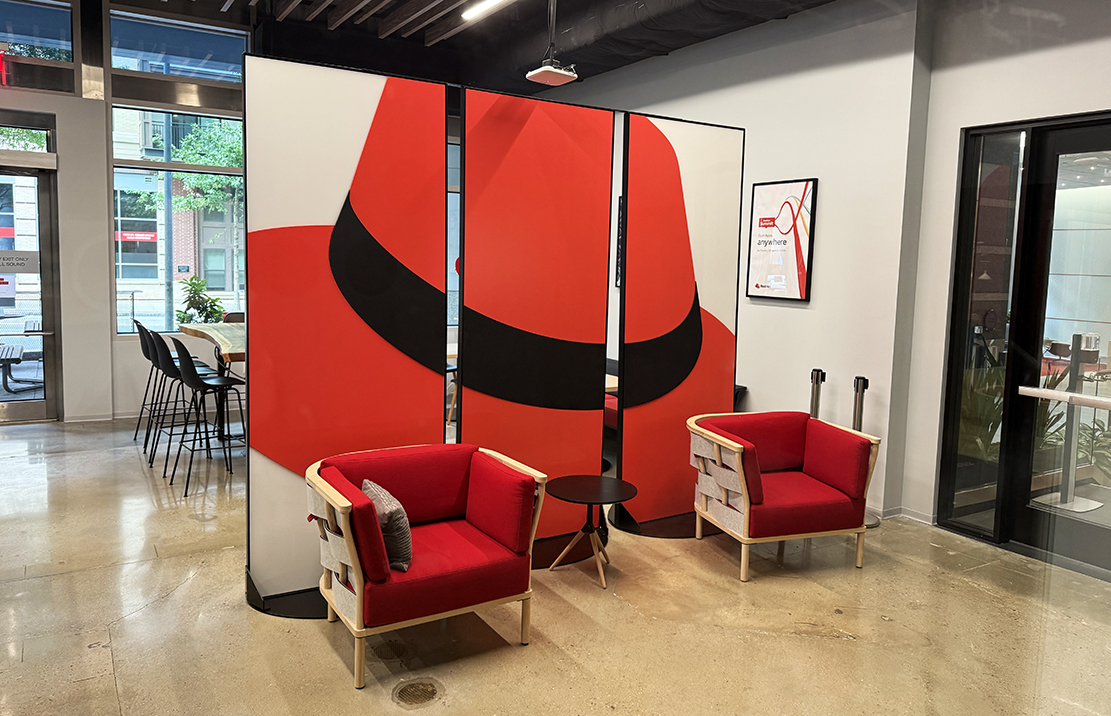 Foto di un paravento alla Red Hat Tower su cui è applicata l'immagine del cappello divisa sui tre pannelli del complemento d'arredo.
