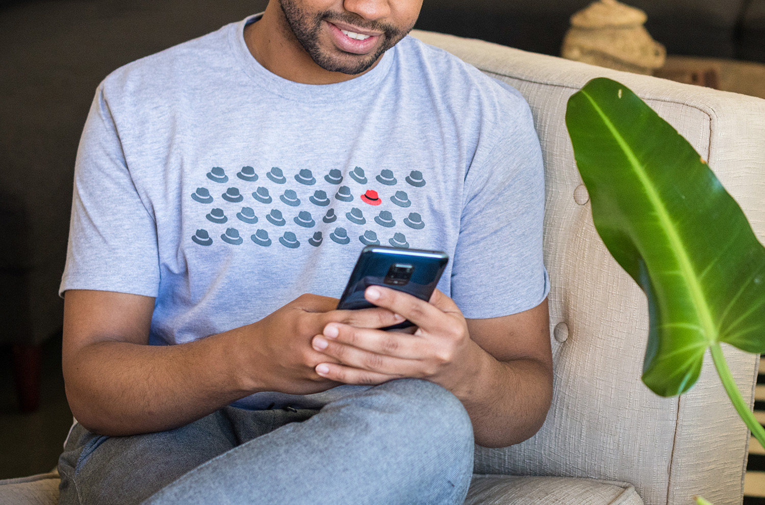 Foto di un uomo con una t-shirt acquistata al Red Hat Cool Stuff Store. L'immagine sulla t-shirt è un motivo formato dalla ripetizione del cappello su più righe. Tutti cappelli sono in versione monocolore grigia, tranne uno che è a colori. Il logo Red Hat completo è stampato sul retro della t-shirt.