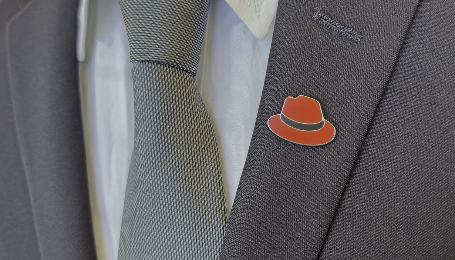 Foto di una spilla a forma di fedora appuntata sulla giacca di un completo.