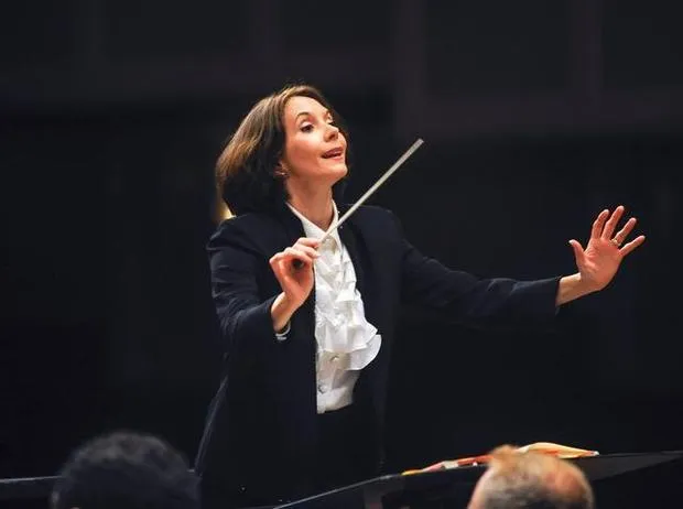 A photograph of a woman in a formal suit conducting an orchestra A photograph of a woman in a formal suit conducting an orchestra